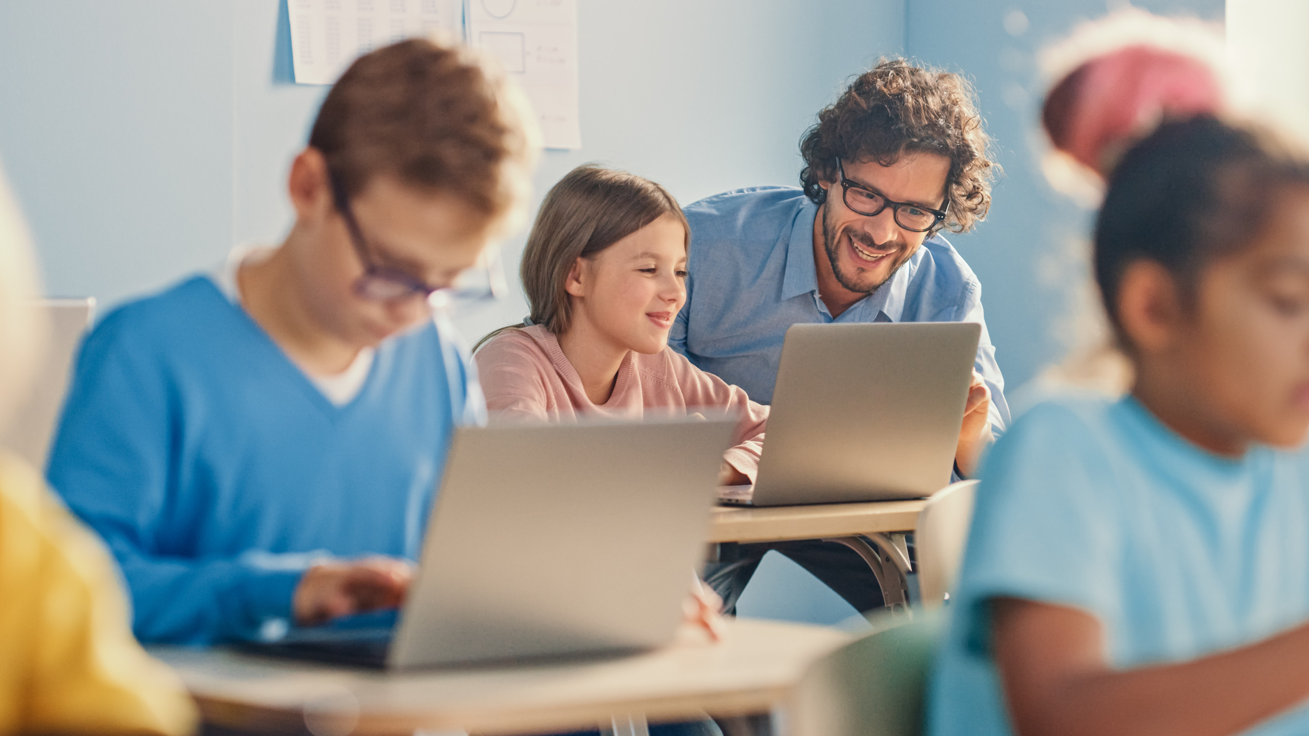 Kinder im Klassenzimmer an ihren Tischen mit ihrem Notebook. Lehrer hilft seiner Schülerin