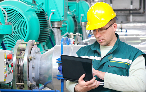 Ingenieur mit Schutzhelm überprüft Maschinen in einer Fabrik mit Tablet